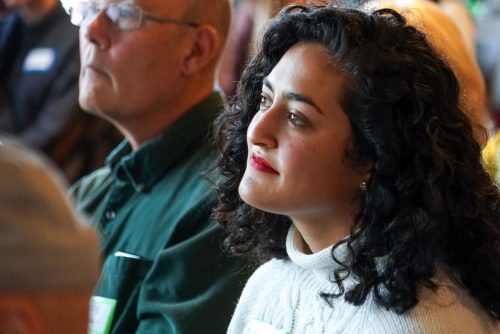 A person sitting in a crowd listening to someone speaking.