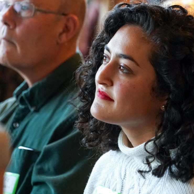 A person sitting in a crowd listening to someone speaking.
