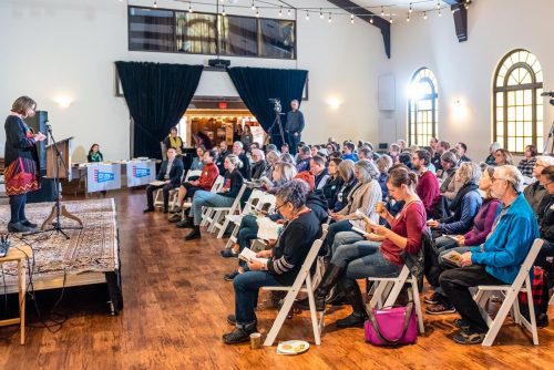 A large room with a crowd of people seated and listening to a person sharing from the stage.