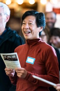 A person holding a printed program and singing.