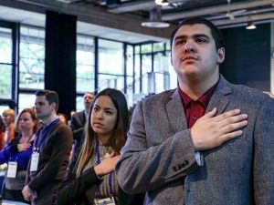 A few people standing with their hands over their hearts.