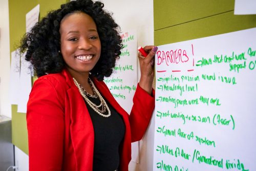 A person standing at the wall with a handwritten poster, holding a pen and smiling.