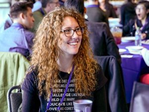 A person sitting at a table with others and smiling.