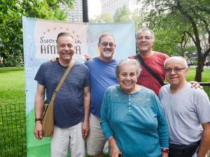 A small group of people standing outside in front of a banner that reads, Sworn-Again America.