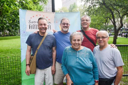 A small group of people standing outside in front of a banner that reads, Sworn-Again America.