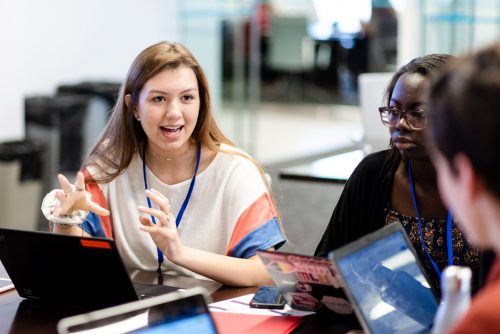 A few young people sitting around their computers and talking.
