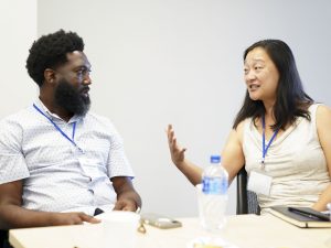 A man and woman are talking while sitting in chairs, at a table.