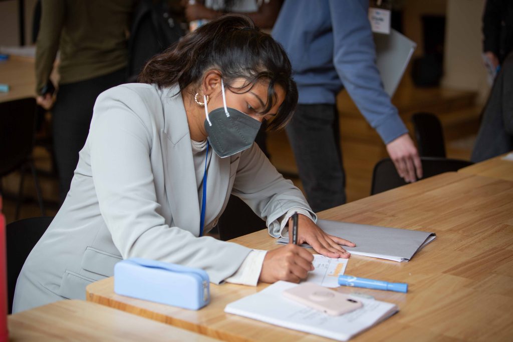 An image of Anishka Durvasula sitting at a table and writing on a notepad.