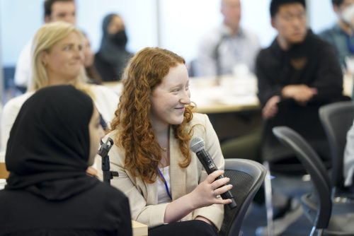 A candid image of YC alumna, Ellie Friedman. Ellie is wearing a tan blazer and is holding a microphone.