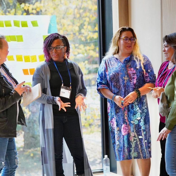 A handful of people speaking together in front of windows.