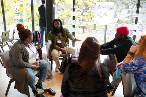 A group photo of Citizen University participants sitting in a circle of chairs, engaging in a discussion.