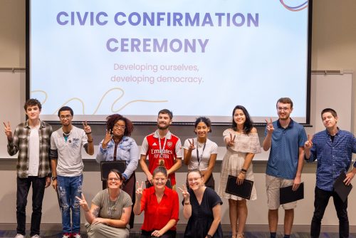 A group of students at the front of a room smiling and holding diplomas. 