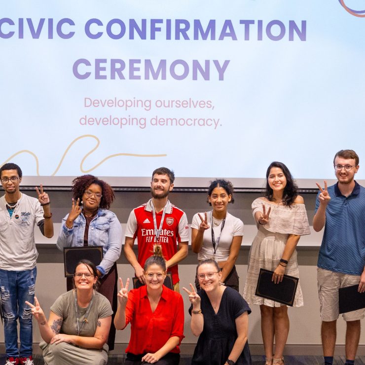 A group of students at the front of a room smiling and holding diplomas. 