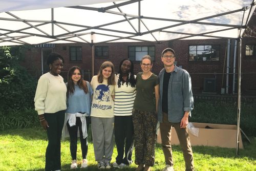 A small group of people standing on a lawn, under a tent.