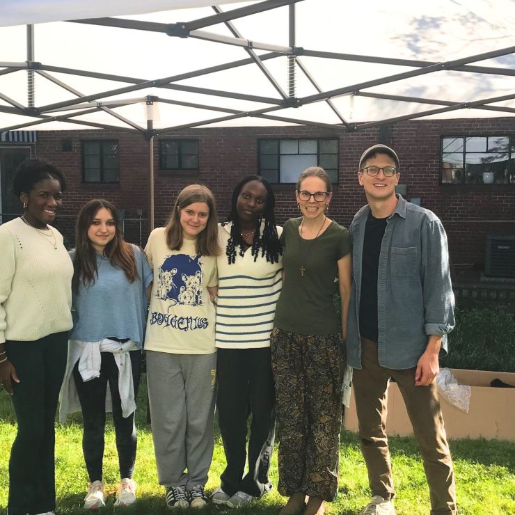 A small group of people standing on a lawn, under a tent.